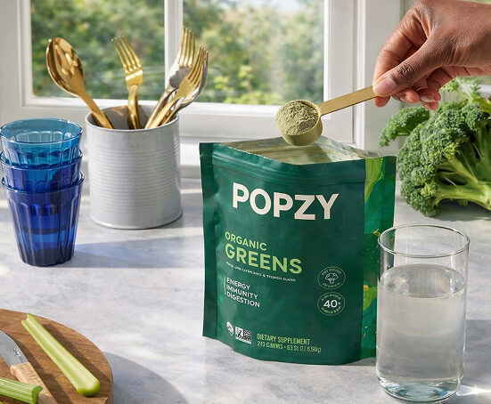 Popzy Organic Greens package on a kitchen counter with a hand holding a scoop of greens.