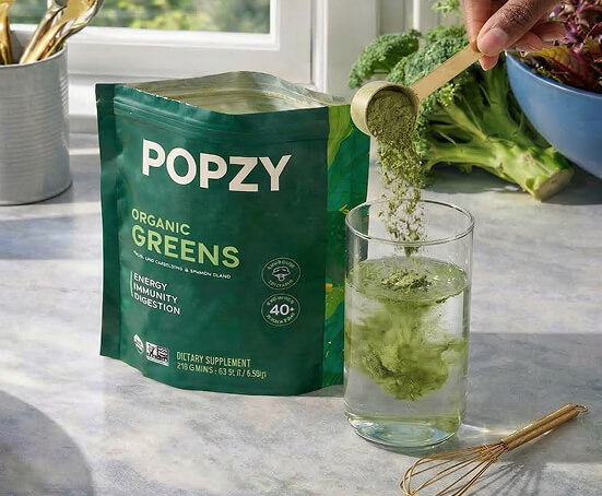 POPZY Organic Greens package with a glass of green liquid on a marble surface.
